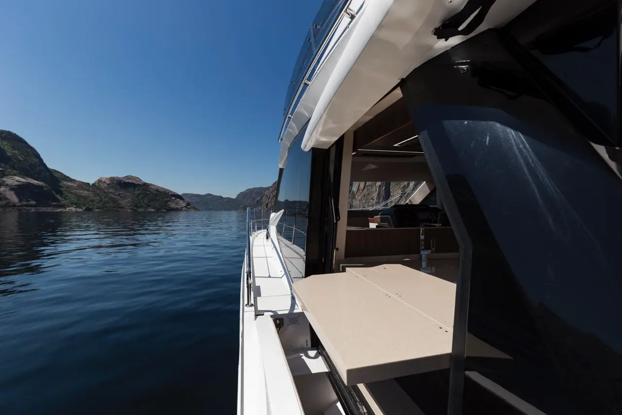 Luxury yacht view with a spacious outdoor table, calm waters, and scenic mountains under a clear blue sky.
