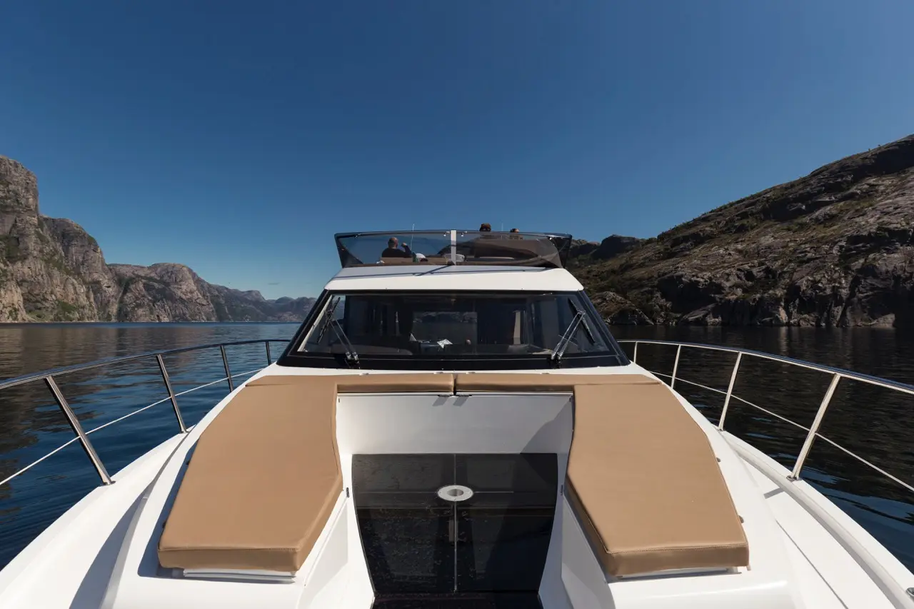 Luxury boat with tan cushions, sailing through calm waters surrounded by cliffs under a clear blue sky.