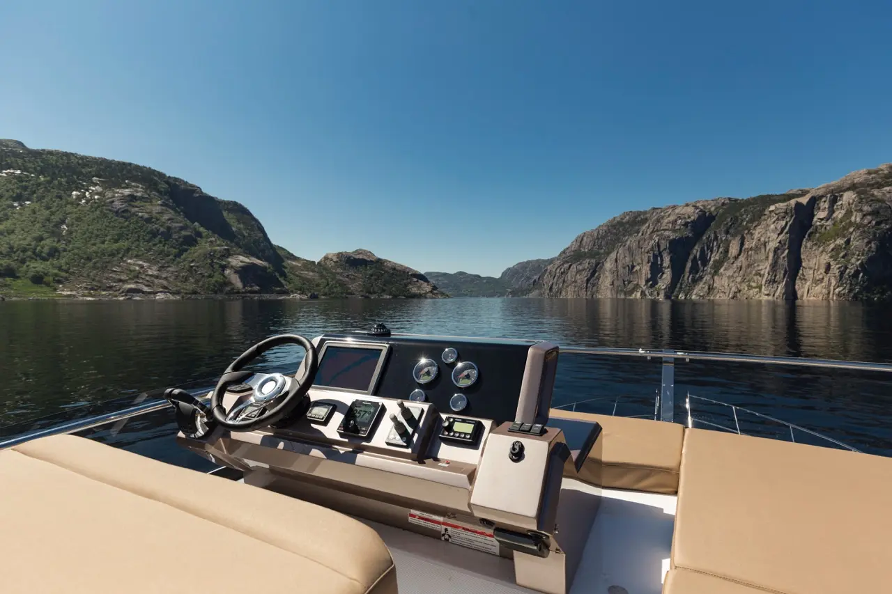 View from a boat's dashboard showcasing a steering wheel, display screen, and scenic cliffs against a clear blue sky.