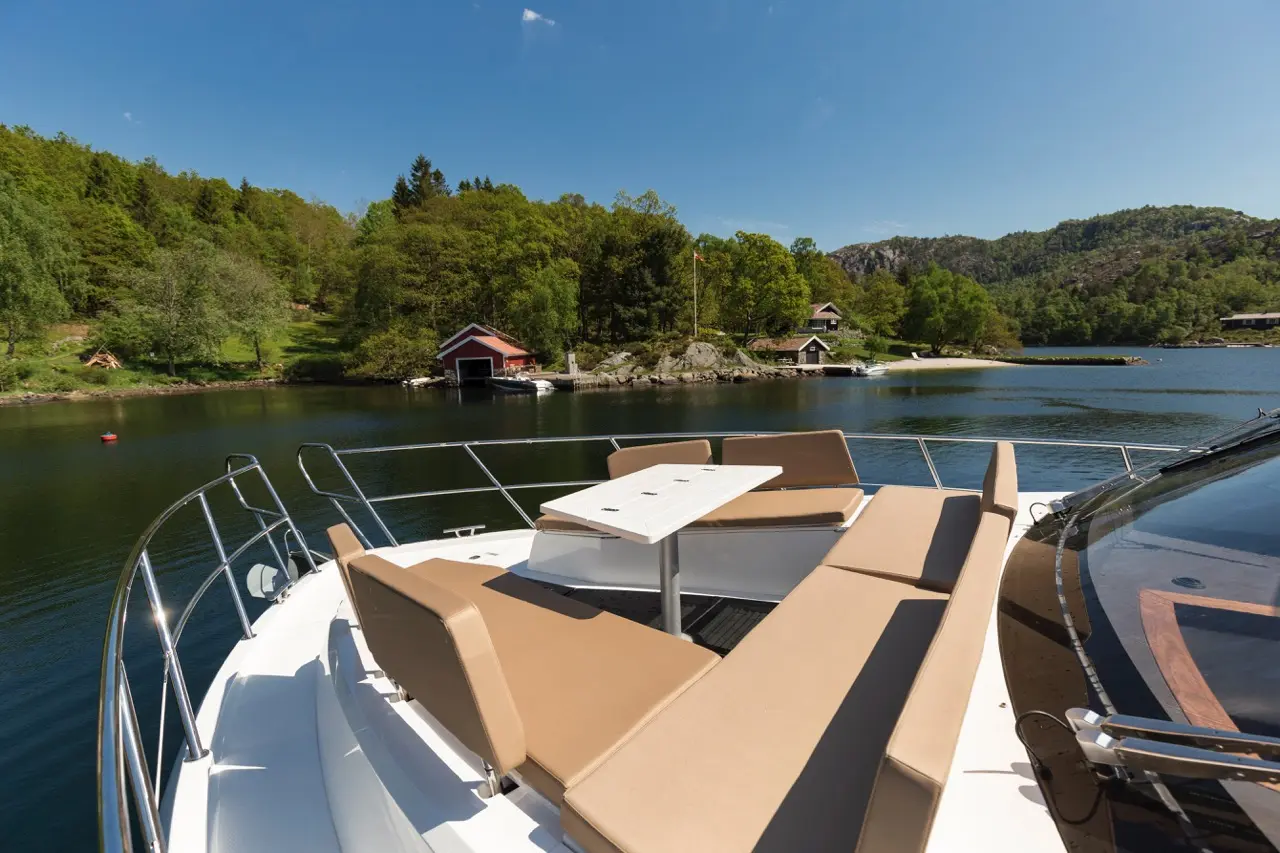Luxury boat deck with beige seating and table, overlooking a serene lake and lush green forest on a sunny day.