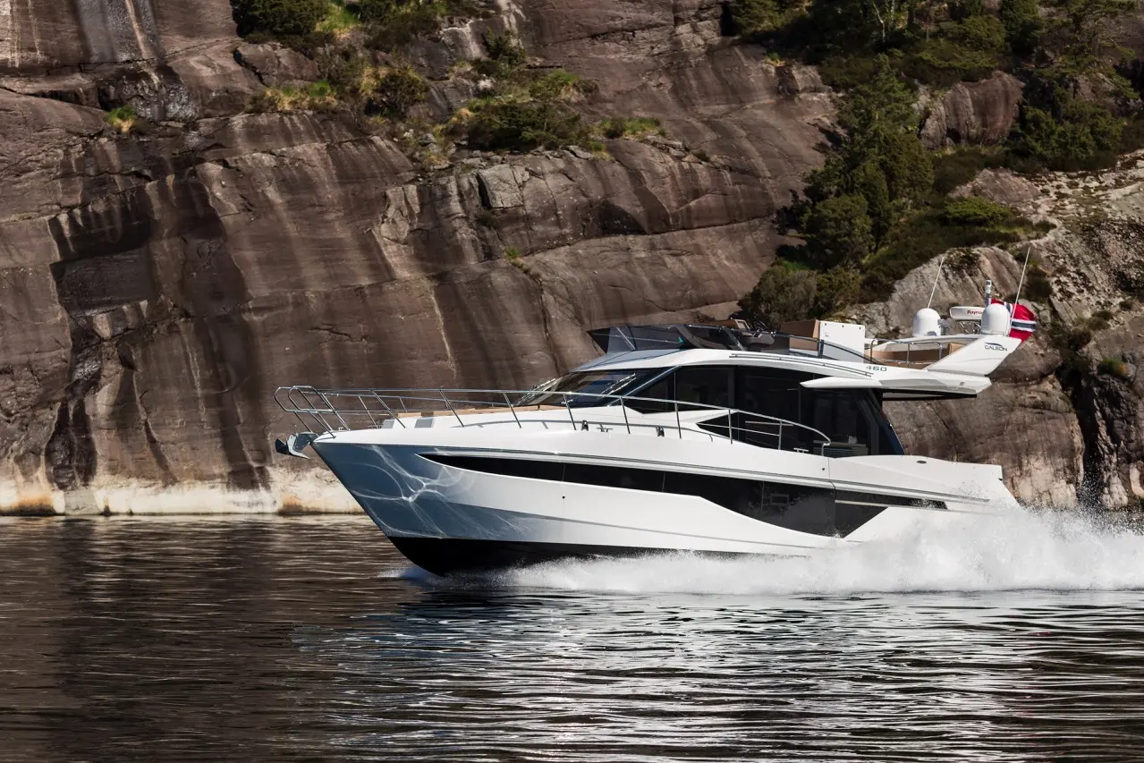 Luxury motor yacht cruising on calm waters near a rocky shoreline, showcasing sleek design and a modern aesthetic.