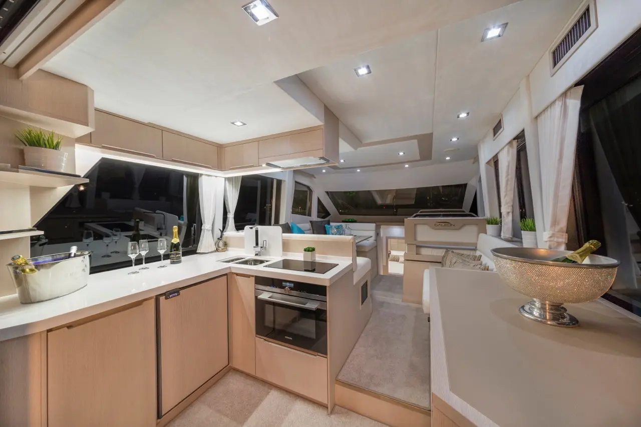 Luxurious yacht interior featuring a modern kitchen, stylish furnishings, and ambient lighting, with views through large windows.