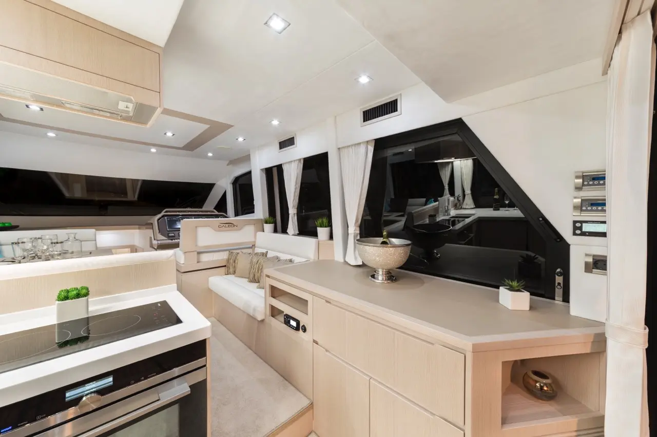 Modern yacht interior with a sleek kitchen, dining area, stylish decor, and large windows, showcasing elegance and functionality.