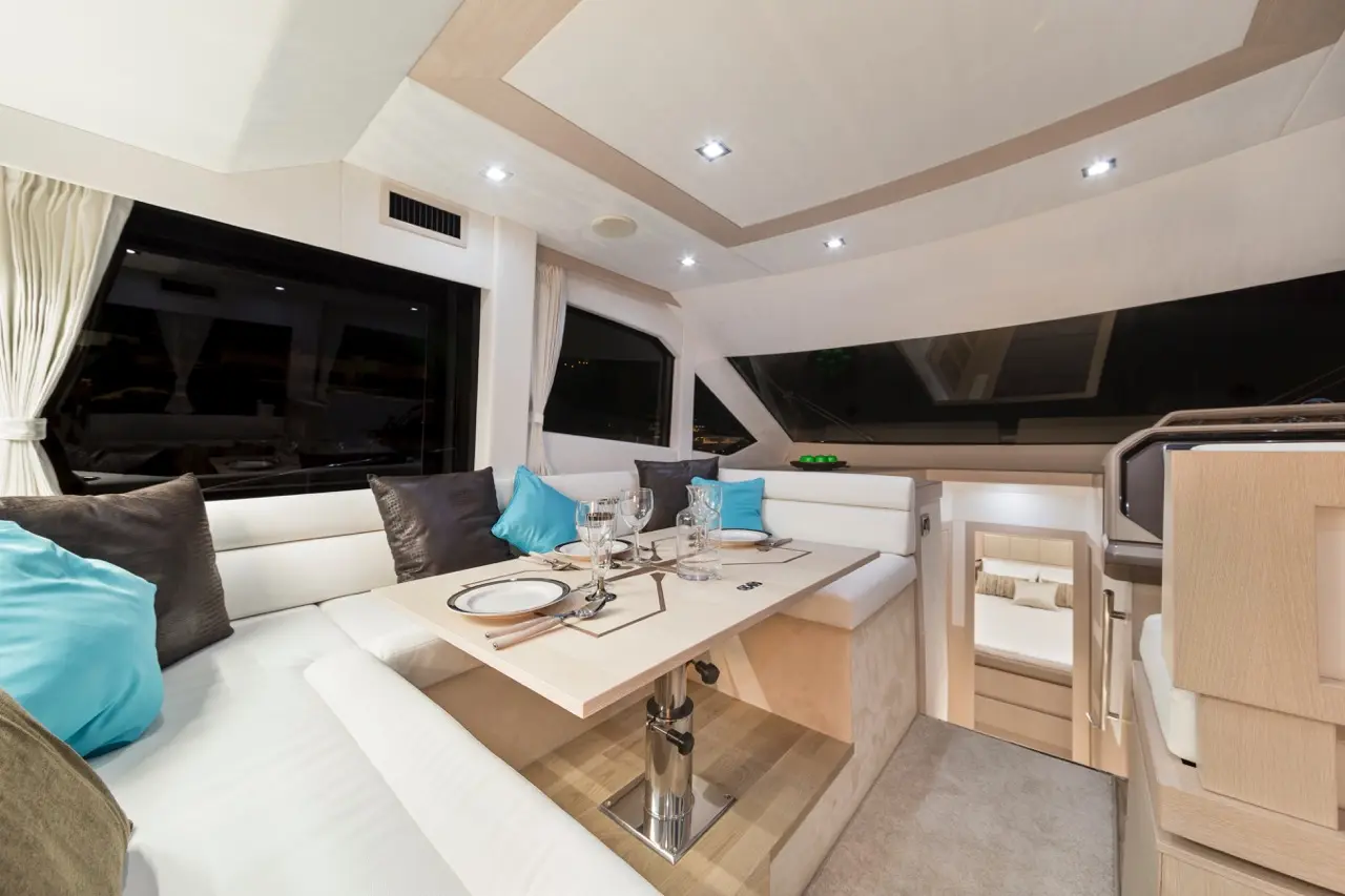 Modern yacht interior featuring a dining area with a table set for dinner, plush cushions, and panoramic windows.