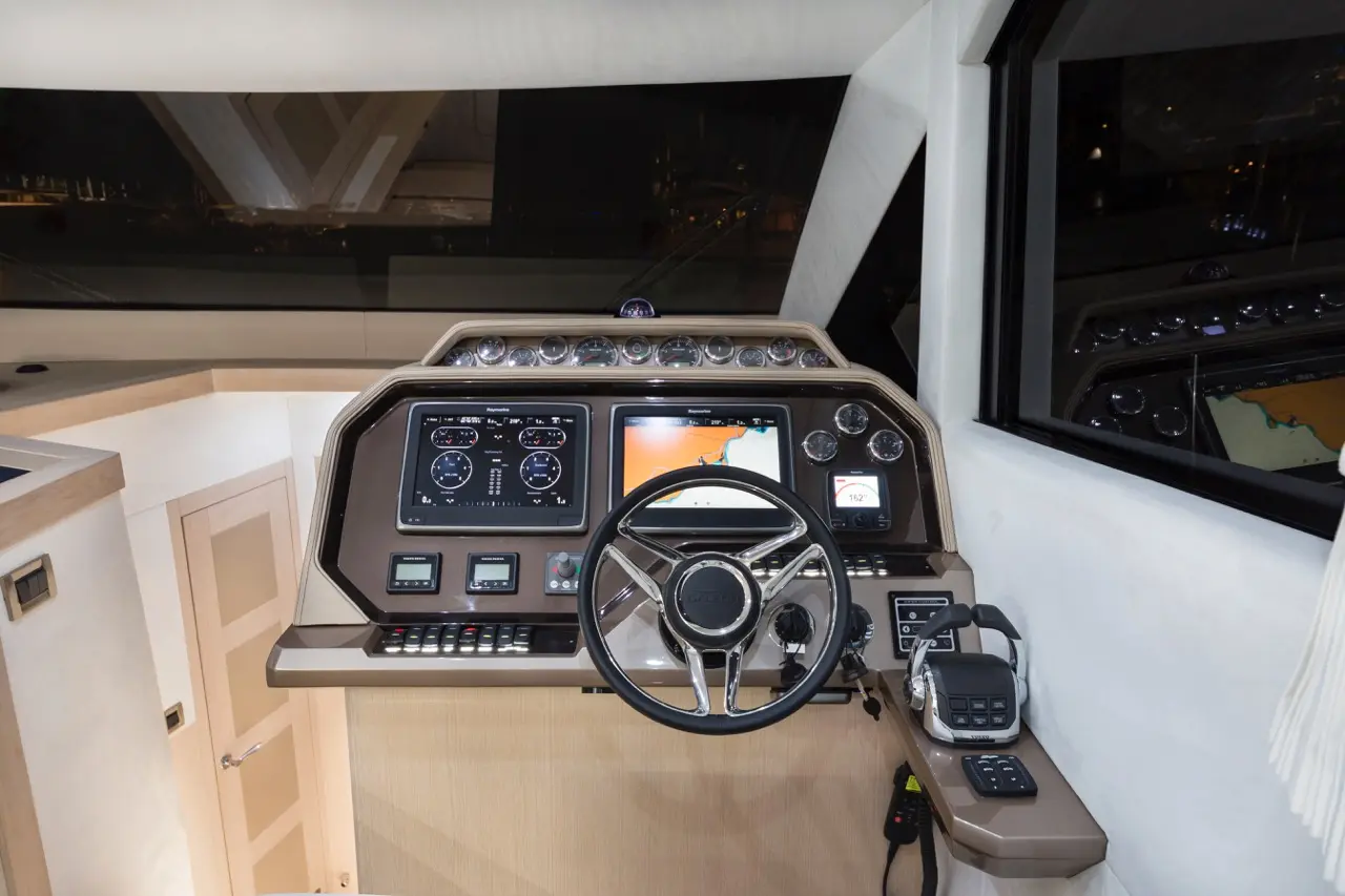 Luxury yacht dashboard view with steering wheel, navigation screens, gauges, and control buttons, showcasing modern design.