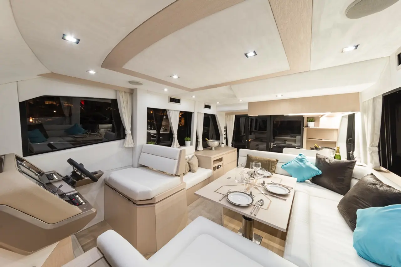 Luxurious yacht interior featuring a dining area, modern furnishings, large windows, and nautical decor under warm lighting.