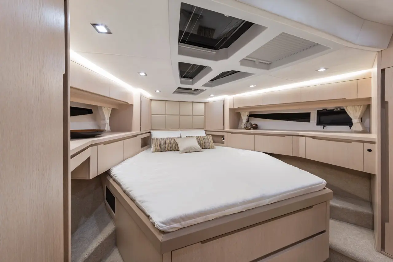 Modern yacht interior featuring a spacious bedroom with a king-sized bed, wooden cabinetry, and soft lighting.