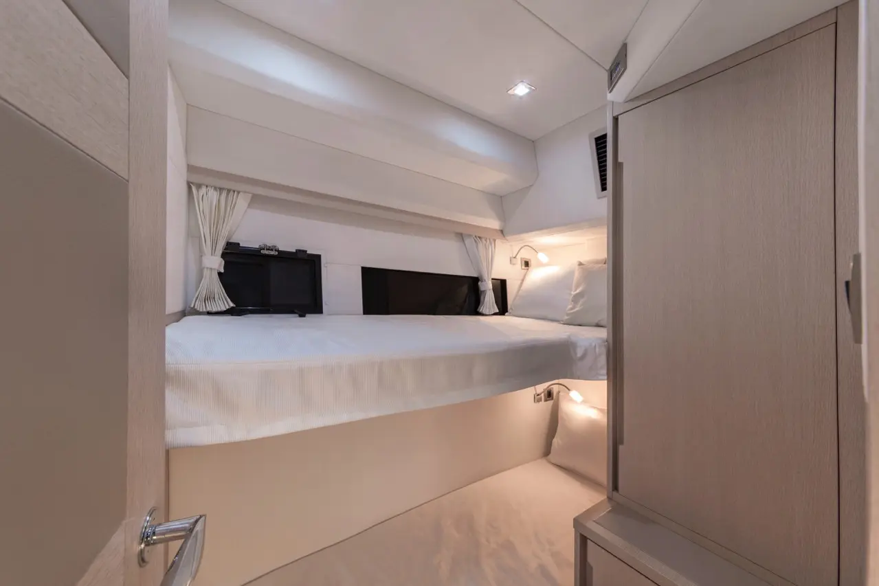 Cozy cabin interior with dual beds, two mounted TVs, and built-in lighting; soft white bedding and modern wood finishes.