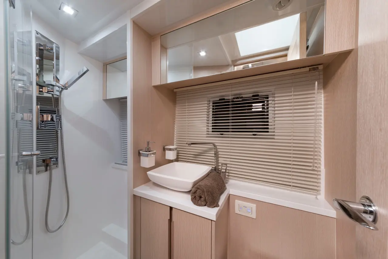 Modern bathroom featuring a shower, basin, towel, and wooden cabinetry, with natural light from a skylight.
