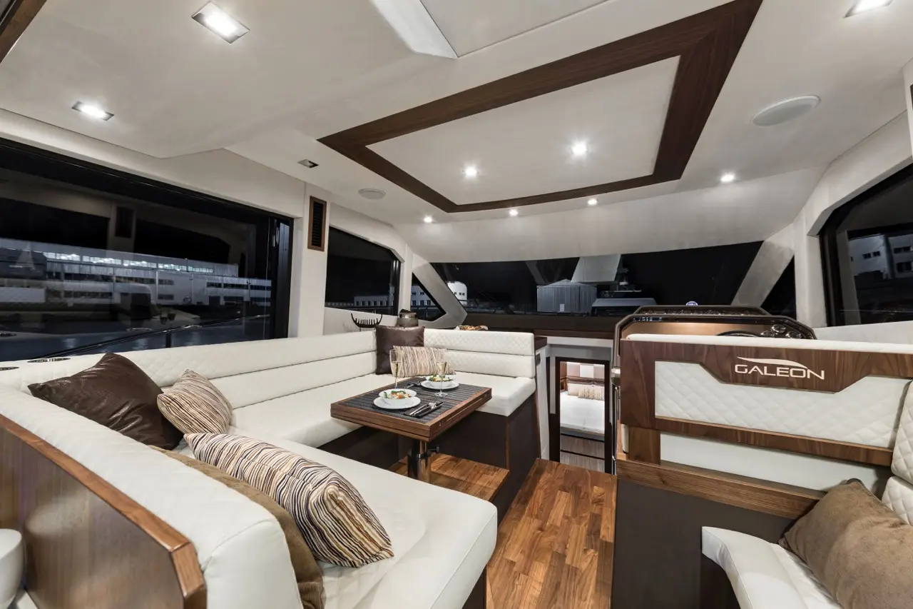 Modern yacht interior featuring a stylish lounge with white seating, wooden accents, and elegant decor. Branding: Galeon.