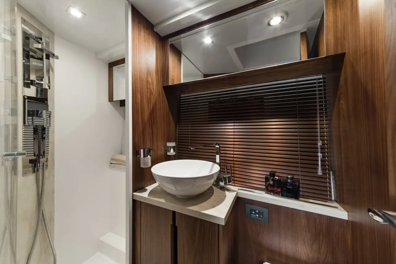 Modern bathroom featuring a sleek round sink, wooden cabinetry, and a glass shower with stylish fittings.