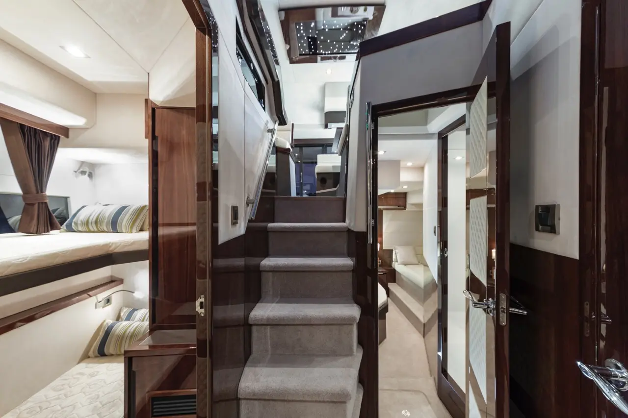 Interior staircase of a luxury yacht with plush carpet, leading to stylish living quarters and sleeping areas, softly lit.