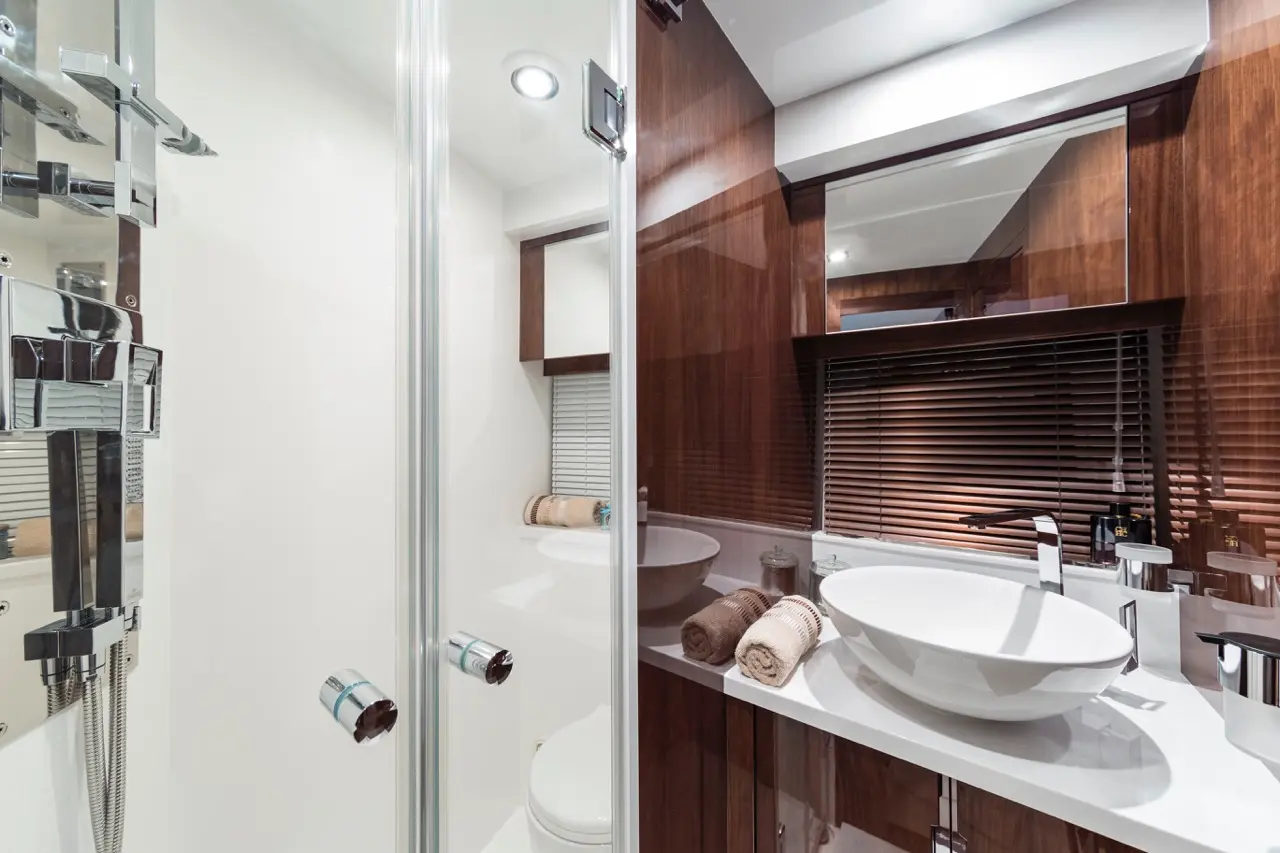 Modern bathroom with glass shower, wooden cabinetry, round sink, and neatly rolled towels on the counter. Soft lighting.