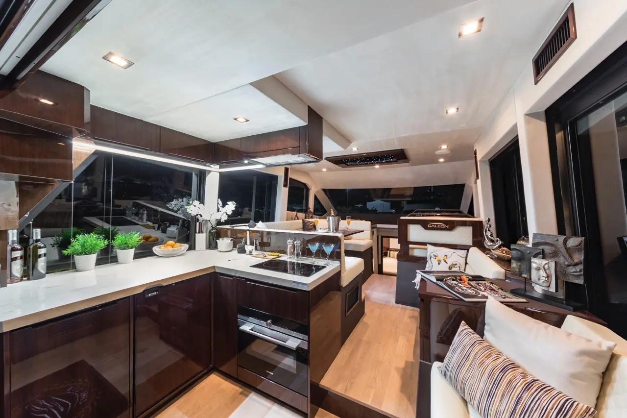 Sleek modern yacht kitchen featuring dark wood cabinets, white marble countertop, potted plants, and views of the water.