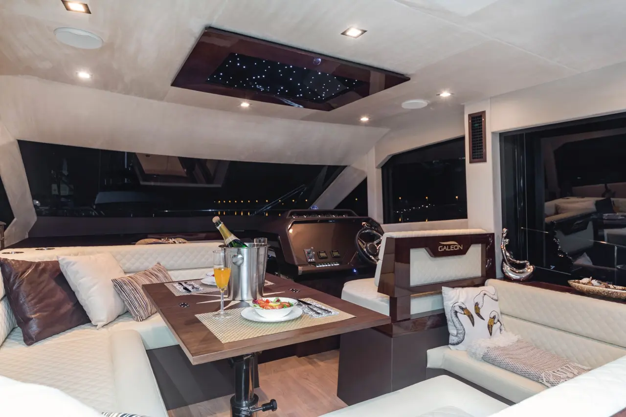 Luxurious yacht interior featuring elegant seating, a table with food and drinks, and a starry skylight glowing at night.