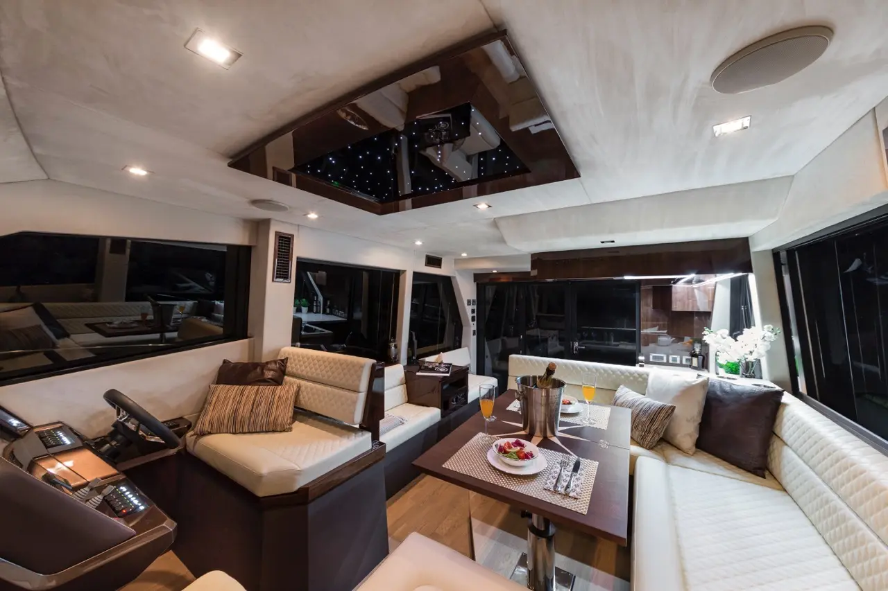 Luxurious yacht interior featuring plush seating, a wooden dining table, and a starry ceiling with drinks and snacks on the table.
