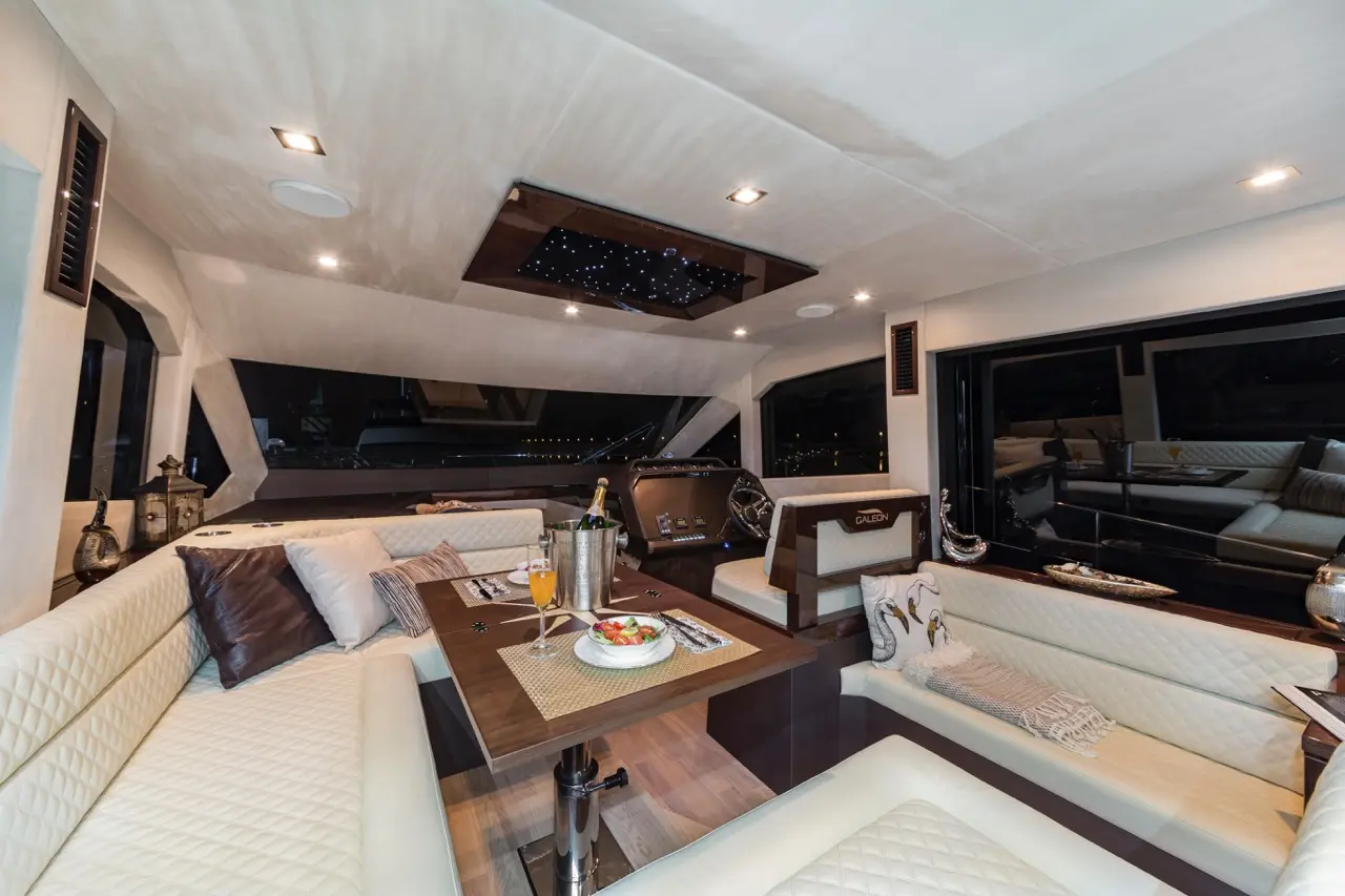 Luxurious yacht interior with plush seating, a wooden dining table set with food, and ambient lighting against night views.