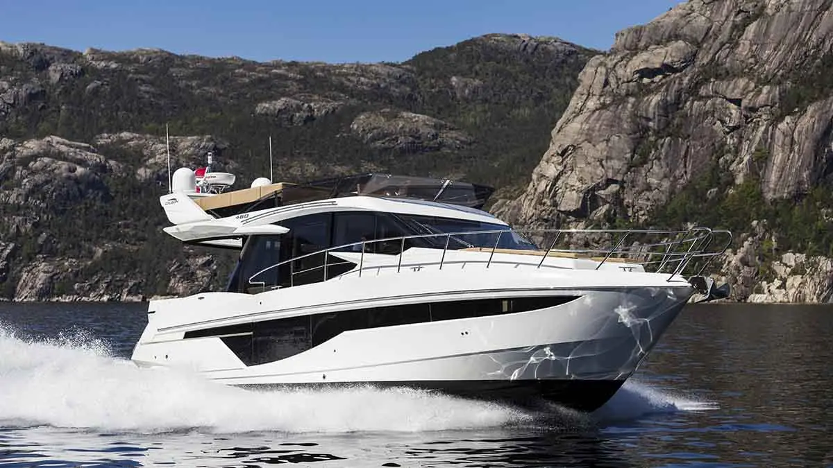 A sleek white yacht speeds through calm waters, flanked by rugged mountains, showcasing luxury and adventure on the sea.