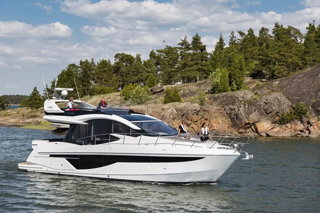 A modern white yacht with passengers wearing life jackets navigating through a tranquil waterway with rocky shores and trees.