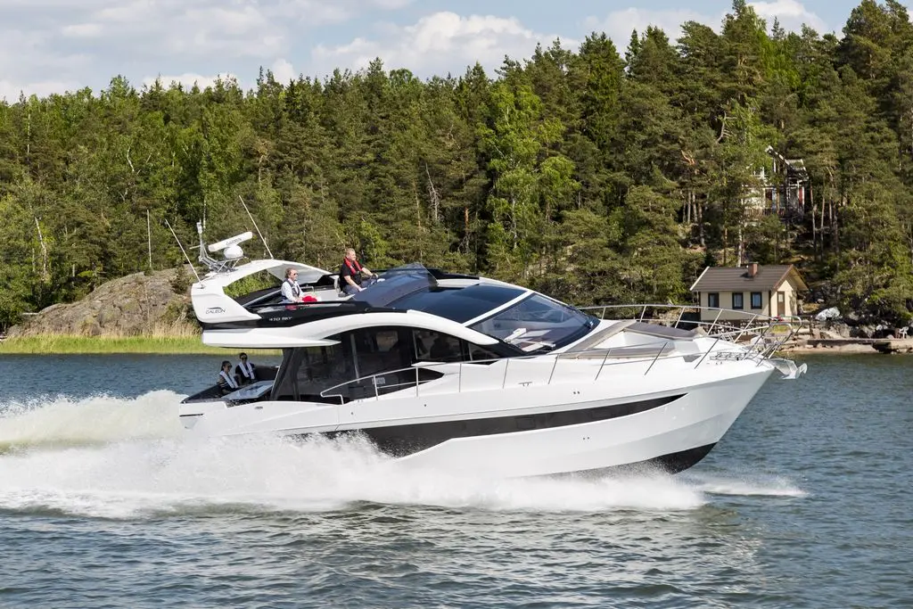 A sleek white motorboat cruising on a lake with passengers enjoying the sunny day and lush green trees in the background.