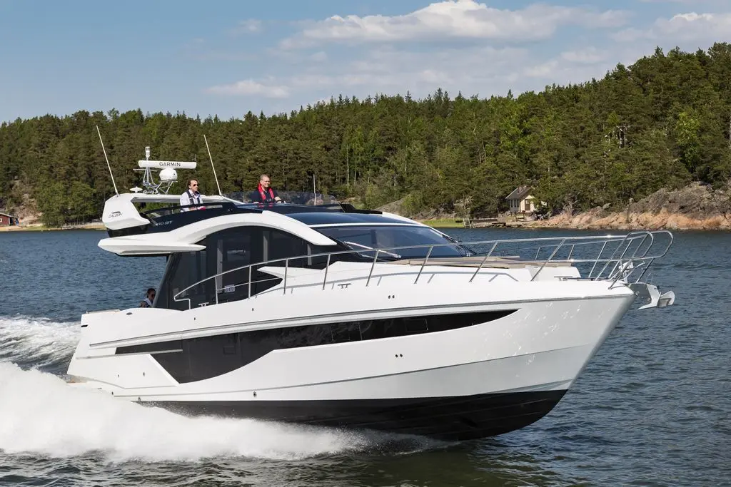 A sleek white motor yacht gliding through calm waters with two men onboard, surrounded by lush greenery and a cozy cabin in the background.