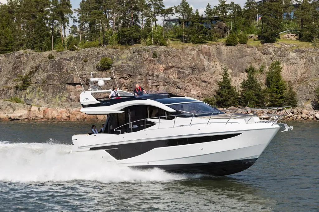 A white motor yacht cruises through calm waters, surrounded by rocky cliffs and trees, with passengers enjoying the ride.