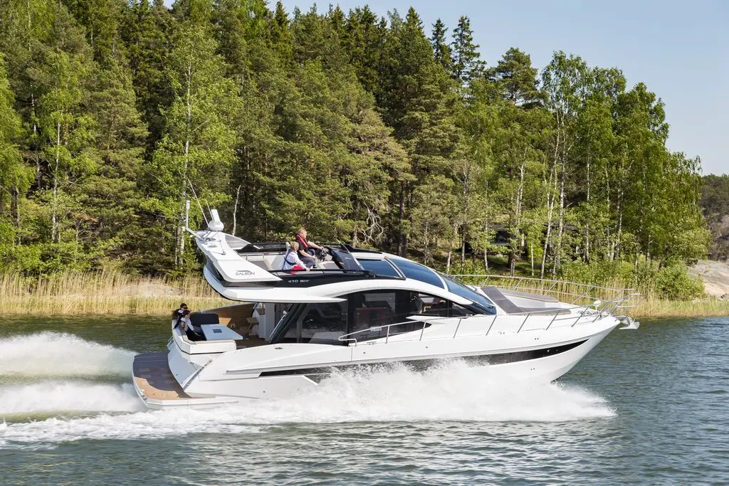 A luxury motorboat speeds through water, with guests enjoying the sun on the deck, surrounded by lush green trees.
