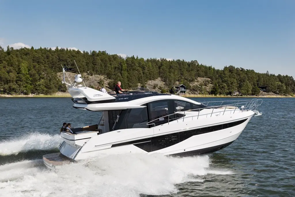 A sleek white and black motor yacht speeds across blue water, with passengers enjoying the ride on a sunny day.