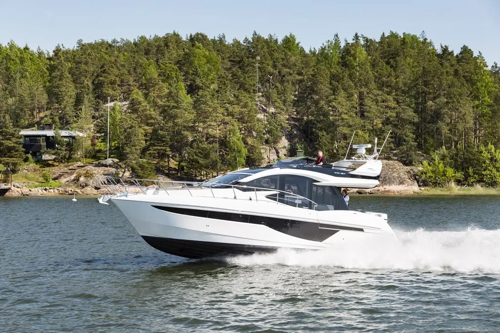 Luxury motor yacht cruising on calm water with green forested shore in the background, showcasing boating lifestyle and leisure.