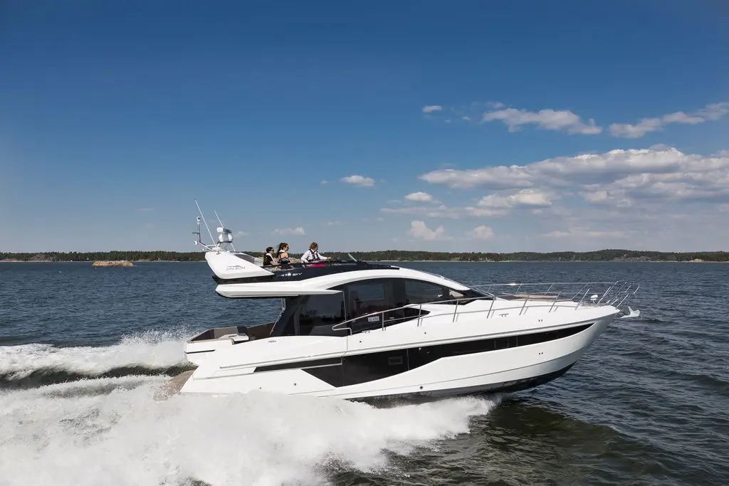 A luxury motor yacht navigates through calm waters, with passengers enjoying the view under a clear blue sky.
