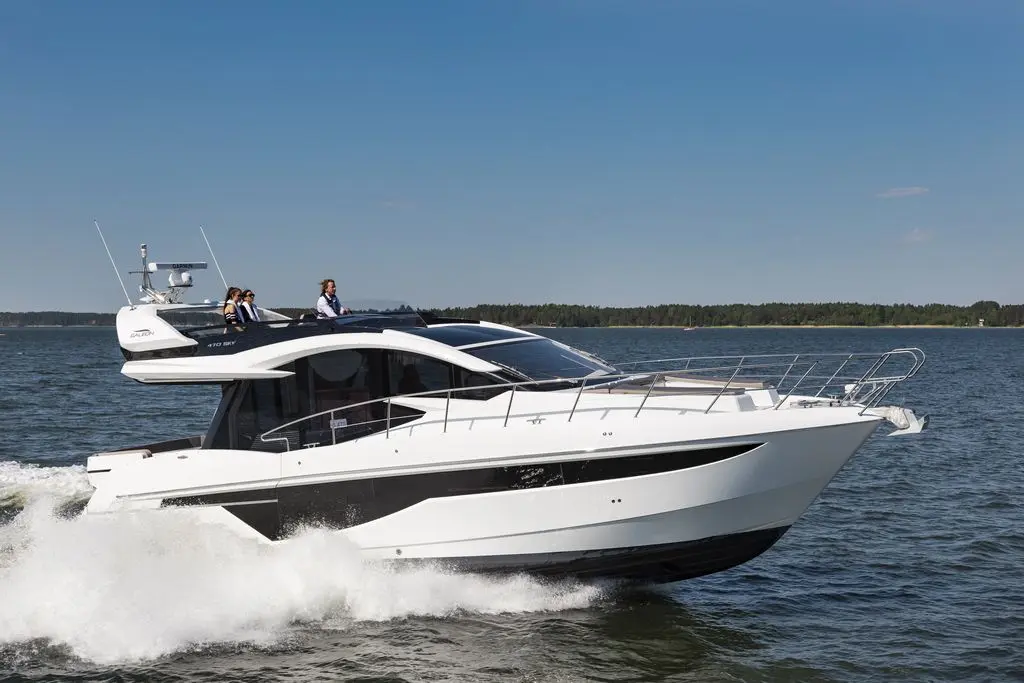A sleek white yacht cruises on blue water, with four people enjoying the ride under a clear sky.
