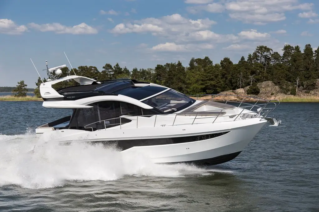 A sleek white motorboat speeds through calm waters, surrounded by green trees and a clear blue sky, showcasing modern design.