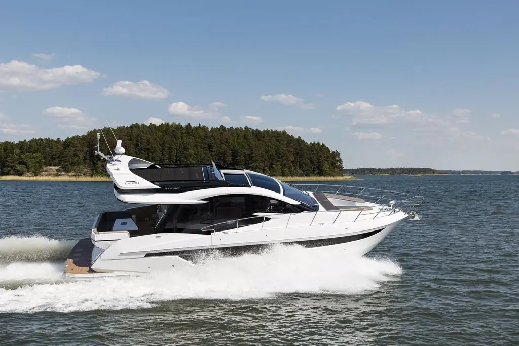 A sleek white motor yacht gliding through blue waters, surrounded by green trees and a clear sky, showcasing luxury boating.