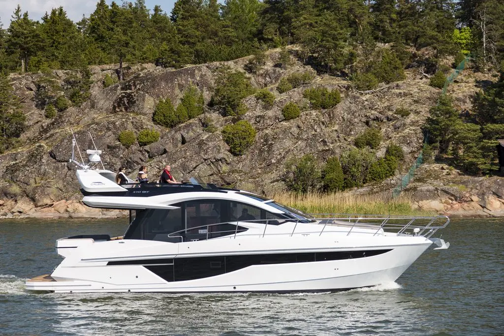 A sleek white motorboat cruises past rocky shores and greenery, with passengers enjoying a sunny day on the water.