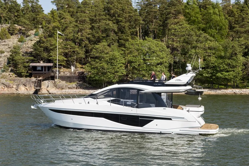A sleek white motor yacht navigates calm waters, surrounded by lush greenery and a wooden dock in the background.