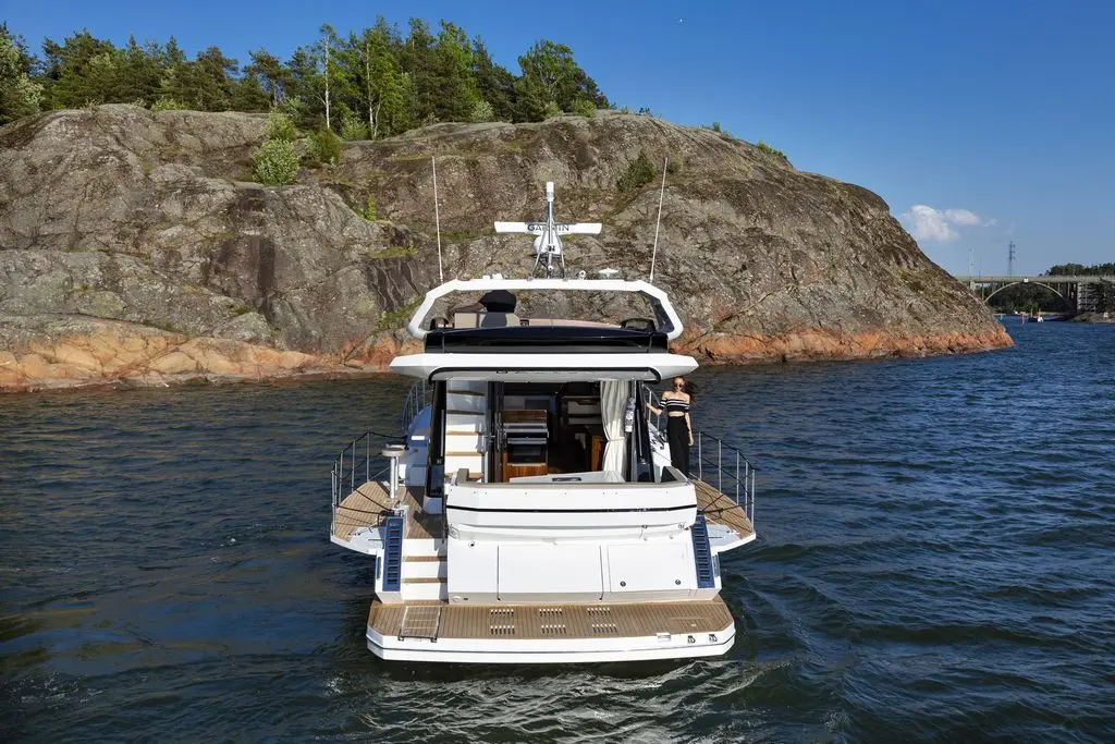 Luxury yacht anchored near rocky shoreline, surrounded by calm water, with a person on board enjoying the view.