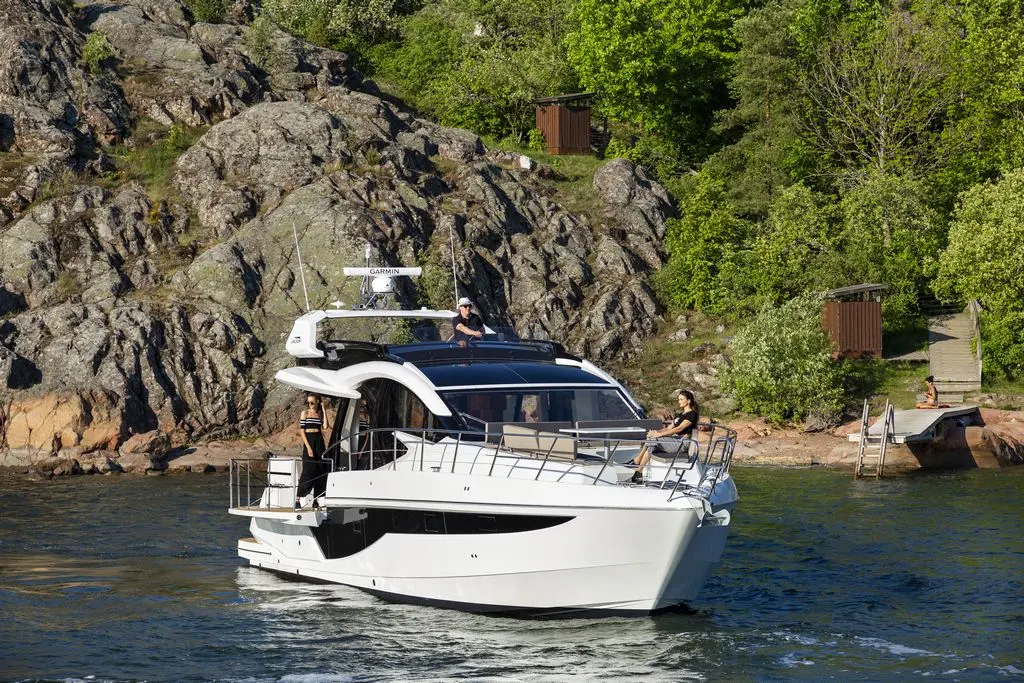 A sleek white motorboat navigates calm waters; passengers enjoy the view near rocky shores and lush greenery.