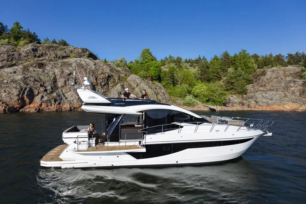 Luxury motor yacht cruising on calm waters, with guests enjoying the sun and scenic rocky coastline in the background.