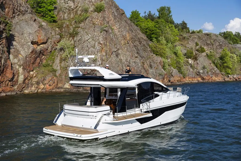 Luxury yacht cruising on calm waters near rocky shores, featuring a modern design and two people onboard.