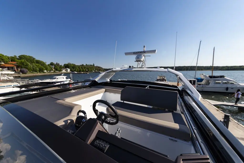 View from the helm of a yacht, featuring a Garmin navigation system, docked by boats and greenery under a clear blue sky.