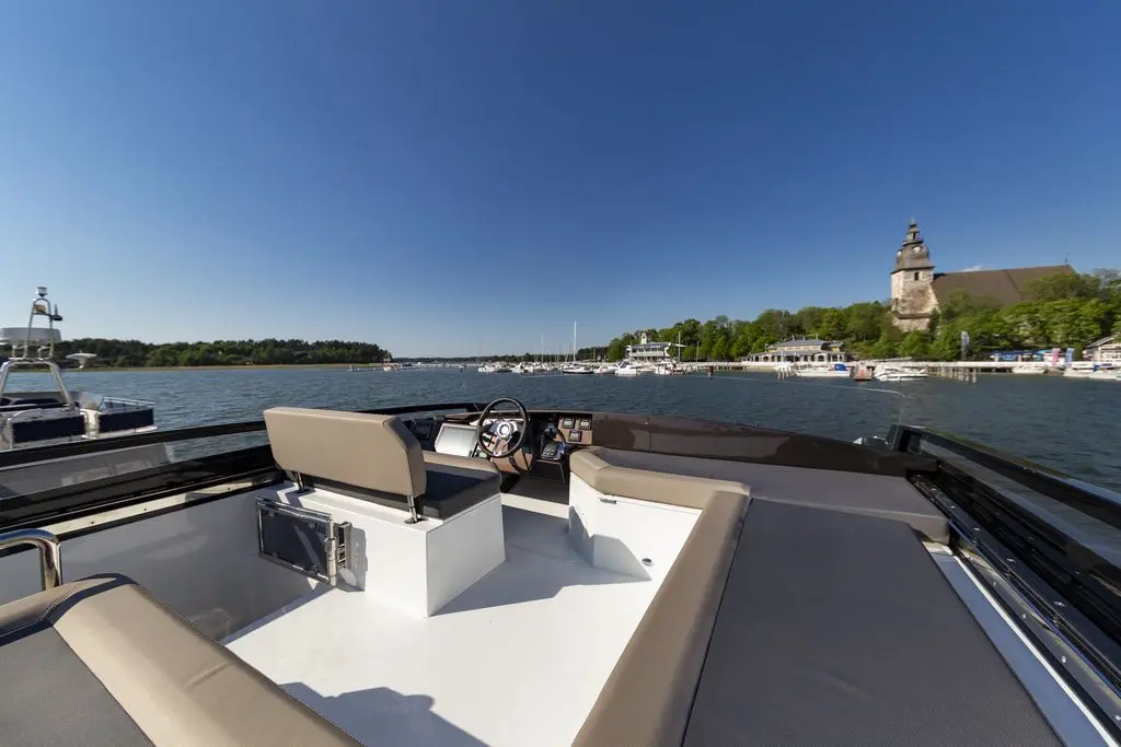 Interior view of a boat on water, showing steering wheel and seating, with a distant view of a riverside church.
