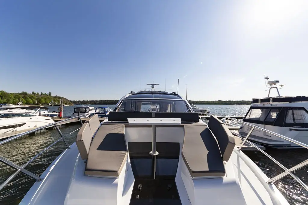 Luxury yacht at a marina with clear blue skies, showing seating on the deck and nearby moored boats.