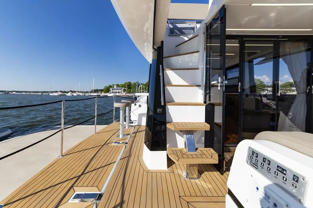 Modern yacht deck featuring wooden flooring, stairs leading to an upper level, and a view of moored boats in the background.