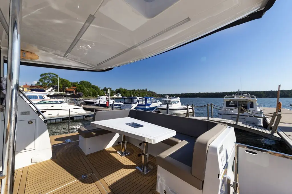 Modern boat deck with a white table and cushioned seating, overlooking a marina filled with various boats under a clear sky.