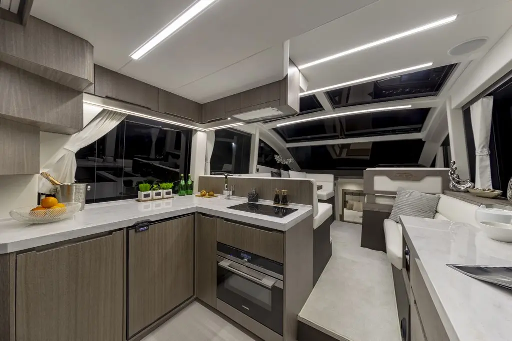Modern yacht interior featuring a sleek kitchen with quartz countertops, appliances, and a cozy seating area, illuminated by LEDs.