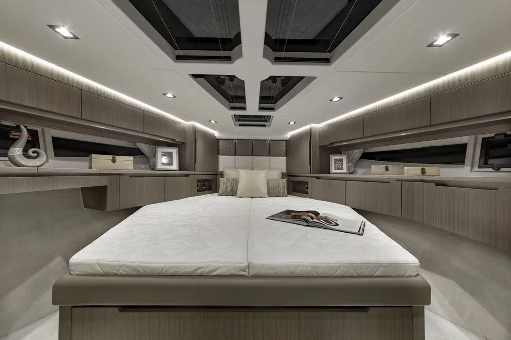 Modern yacht cabin interior featuring a queen-size bed, decorative pillows, wood cabinetry, and ambient lighting.