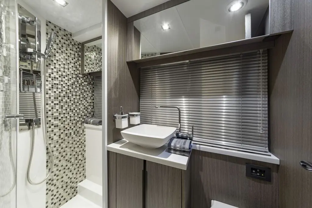 Modern bathroom with tiled walls, a basin, mirror, and shower area, featuring sleek fixtures and towel storage.