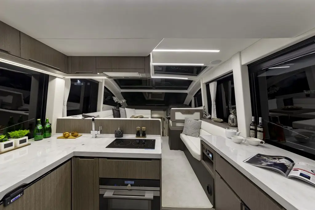 Modern yacht interior featuring a sleek kitchen with marble countertops, ample seating, and shelves with green plants and beverages.