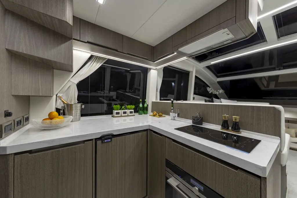 Modern yacht kitchen featuring dark wood cabinetry, quartz countertops, induction cooktop, fruit bowl, and decorative green plants.