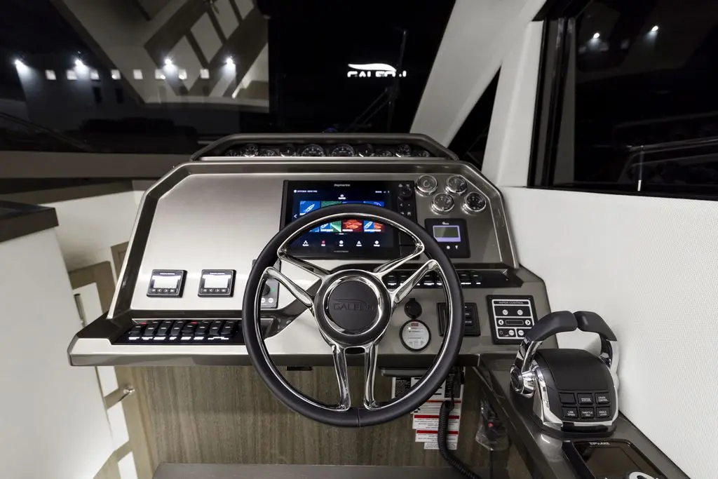 Modern yacht helm with a sleek steering wheel, multifunction display, and various control buttons illuminated at night.